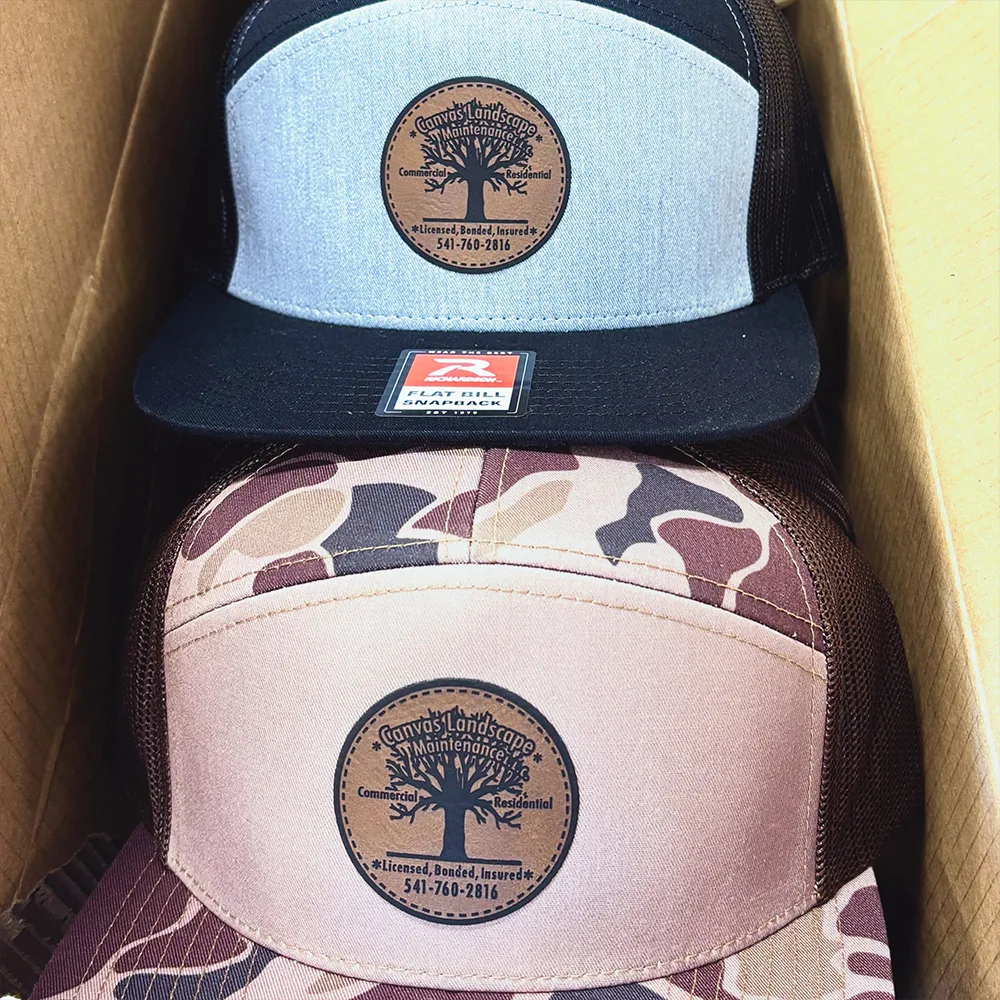 Laser-etched leather patches applied to two trucker caps for a landscaping company