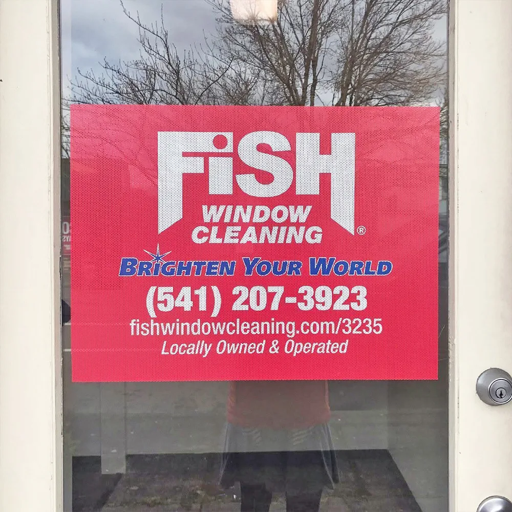 Perforated one-way-vision graphic applied to a glass entry door, showing a printed logo and phone number with the interior visible through the film