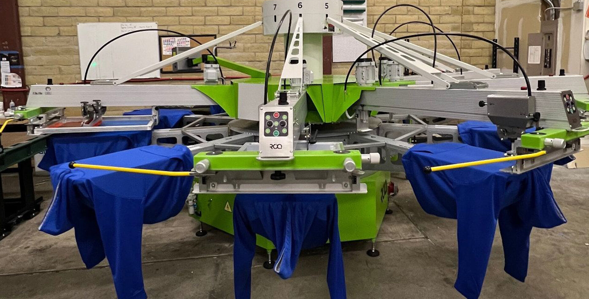 A screen printing press mid-run with blue shirts loaded on the platens at Corvallis Custom
