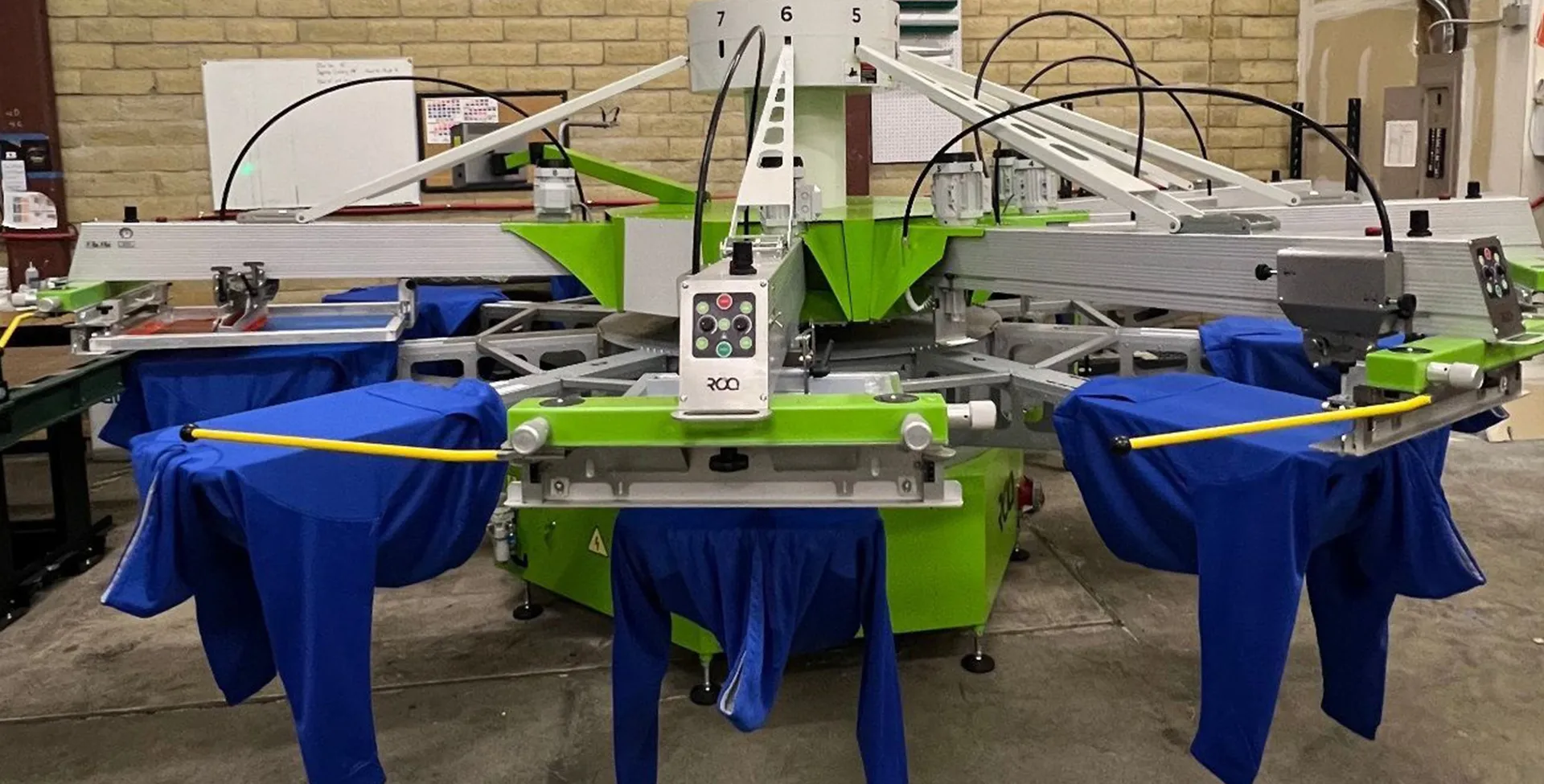 A screen printing press mid-run with blue shirts loaded on the platens at Corvallis Custom