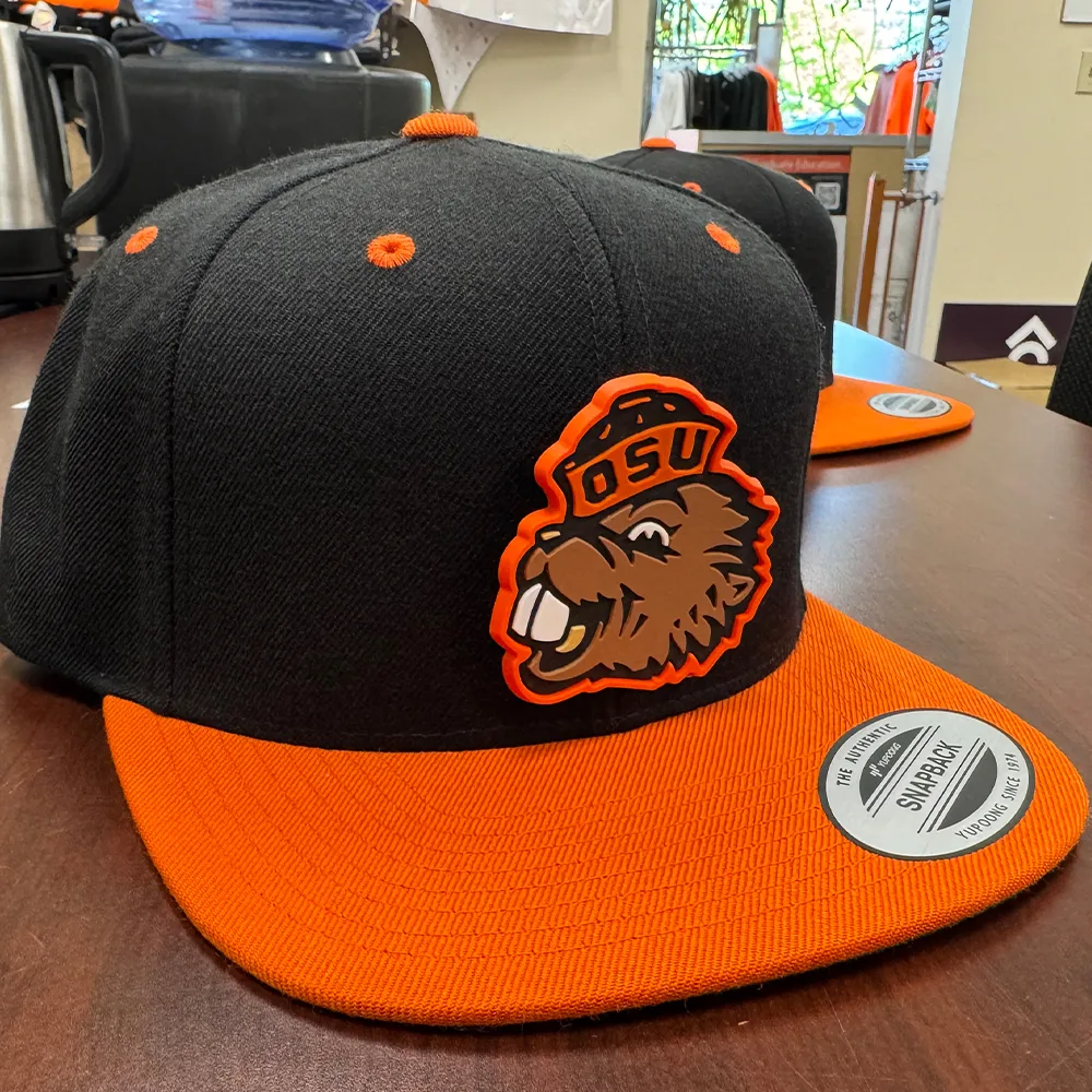 Moulded PVC patch of a beaver mascot applied to a black and orange snapback cap