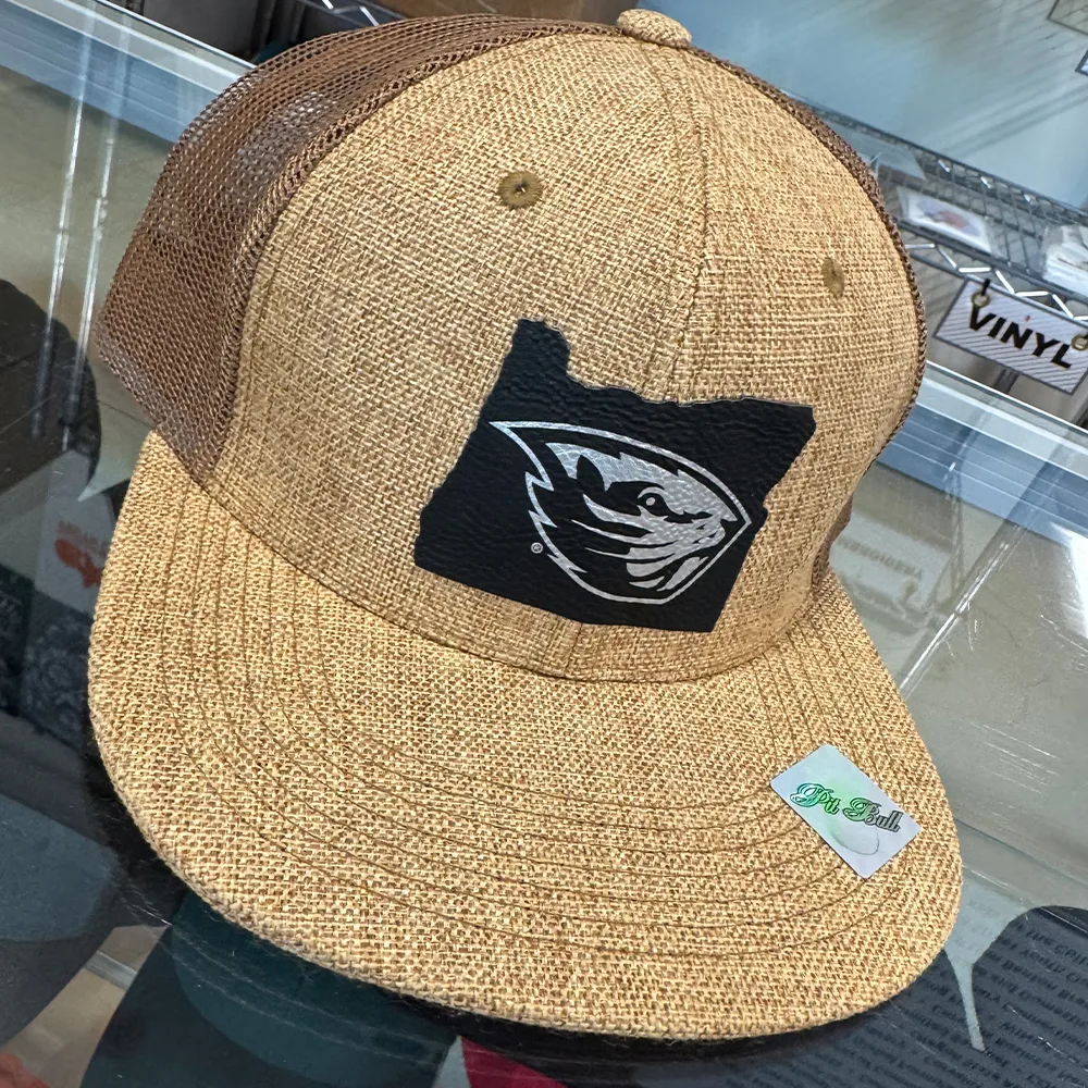 Leather patch with a metallic mascot mark on a burlap-textured trucker cap