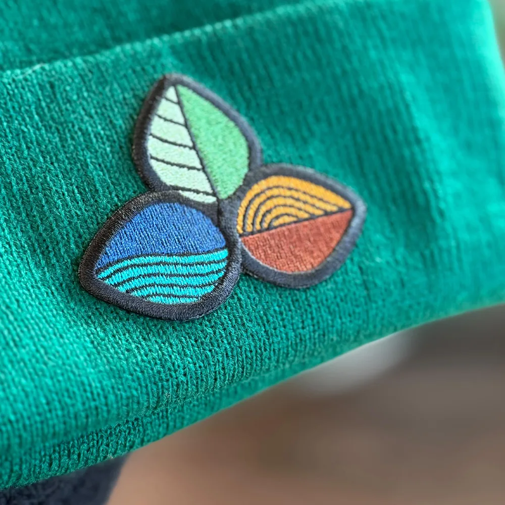 Embroidered stitched patch applied to the cuff of a green knit beanie